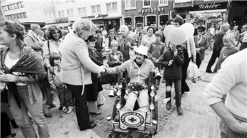 Schwarz-Weiß-Foto zeigt Rollstuhlfahrer umringt von Menschen. Einige gratulieren.