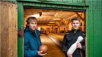 Scheune mit Kegelbahn, im Vordergrund zwei Menschen 
