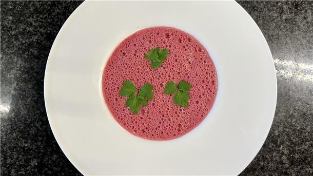 Ein weißer Teller mit pinker Rote Bete Suppe, garniert mit drei Blättern Petersilie. 