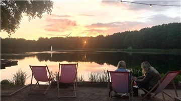 Zwei Frauen sitzen auf Liegen und betrachten den Sonnenuntergang über dem Spekenbütteler Park.