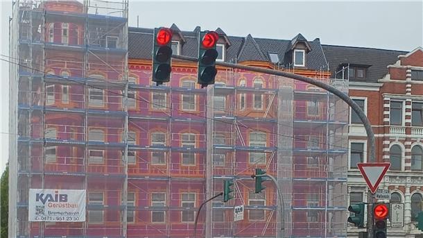 Das Haus in der Hafenstraße Ecke Eupener Straße mit dem ersten, lila-orangefarbenen Anstrich, der trotz des Gerüstnetzes gut erkennbar ist. Das Haus wurde danach neu gestrichen.