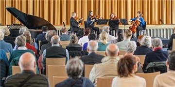Vier Musiker mit Streichinstrumenten spielen in einem Saal vor Publikum.