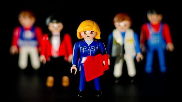 Eine weibliche Playmobil-Figur steht vor mehreren männlichen Figuren.