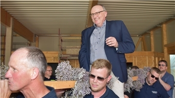 Eine Gruppe Männer trägt einen Richtfestbalken, auf dem ein Mann sitzt.