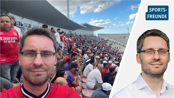 Ein Mann mit rotem Trikot in einem Stadion. Hinter ihn sind Zuschauer zu sehen.