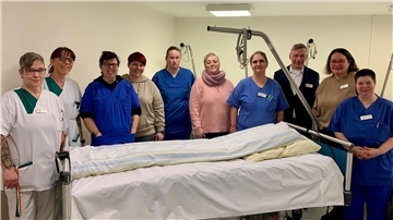 Zehn Menschen stehen hinter einem Krankenhausbett.