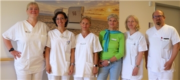 Sechs Mitarbeiter eines Krankenhauses stellen sich zum Gruppenfoto auf. Alle sind in weißer Kleidung zu sehen, bis auf die dritte Person von rechts - die trägt ein grünes Oberteil und eine Jeans. Das Team der Schmerztherapie am Klinikum Bremerhaven-Reinkenheide (KBR) bietet nun stationäre Behandlung auf der neuen Station 2A – mit multiprofessioneller Unterstützung und ganzheitlichem Ansatz.