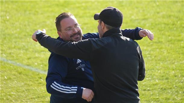 Zwei Trainer am Spielfeldrand klopfen einander anerkennend auf die Schulter.