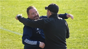 Zwei Trainer am Spielfeldrand klopfen einander anerkennend auf die Schulter.