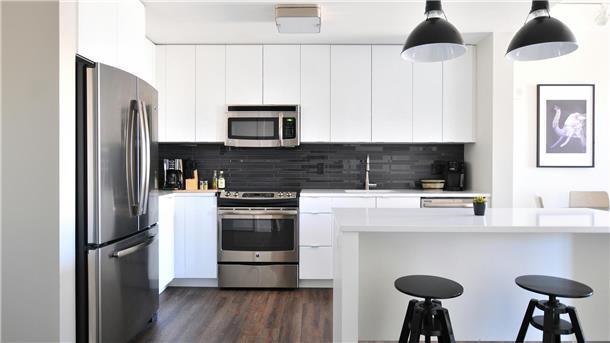 5 Tipps für ein sauberes Zuhause im Herbst Eine moderne, helle Küche mit weißen Fronten und schwarzen Lampen sowie Barhockern.