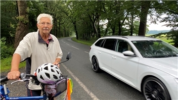 Ein Mann steht mit seinem Fahrrad neben einer Landstraße.