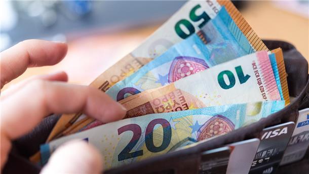 Eine Frau hält eine Geldbörse mit zahlreichen Banknoten und Bankkarten in der Hand.