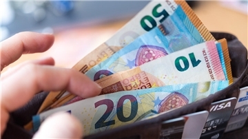 Eine Frau hält eine Geldbörse mit zahlreichen Banknoten und Bankkarten in der Hand.