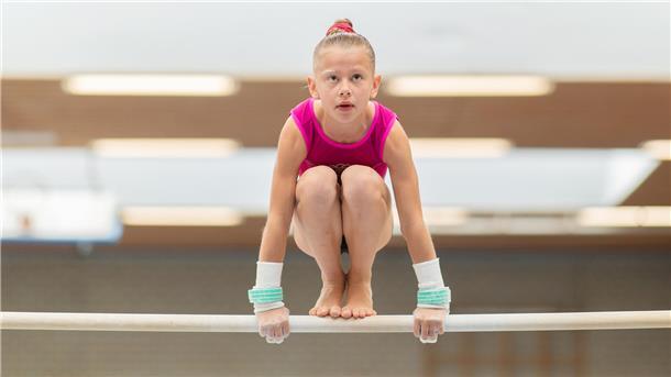 Eine junge Turnerin hockt auf dem Stufenbarren.
