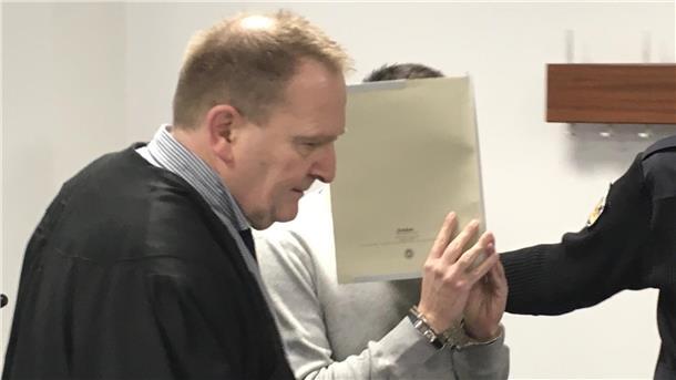 Der 21 Jahre alte Angeklagte wird in den Gerichtssaal geführt und versteckt sein Gesicht.