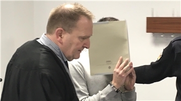 Der 21 Jahre alte Angeklagte wird in den Gerichtssaal geführt und versteckt sein Gesicht.