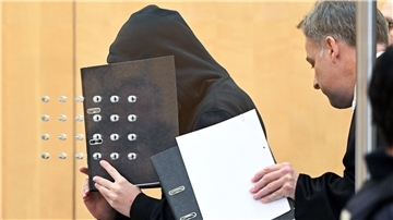 Der Angeklagte (l) verdeckt mit einem Aktenordner sein Gesicht, als er mit seinem Verteidiger zu Beginn der Verhandlung in einem Saal am Oberlandesgericht eintrifft.
