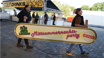 Zwei Frauen tragen in Bramel ein Schild mit der Aufschrift Mittsommernachtsparty.