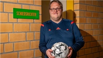 Ein Mann mit Ball vor der Kabine für Schiedsrichter.