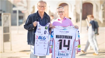 Zwei Männer blicken in die Kamera. Jeder hält ein Trikot in den Händen.