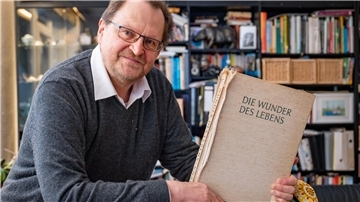 Ein Mann hält das Buch "Die Wunder des Lebens" in der Hand.