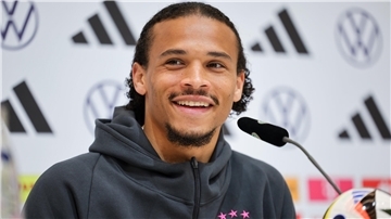 Nationalspieler Leroy Sané sitzt auf einem Podium und spricht mit Medienvertretern. 
