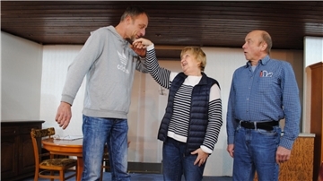 Der entflohene Sträfling Kutte Kaminski (Christian Wellbrock, links) küsst charmant die Hand von Ursula Fischer (Brunhild König), während ihr Mann (Martin Danne) verblüfft und ungläubig zuschaut.