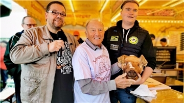 Drei Männer stehen nebeneinander, einer hält einen Schweinskopf.