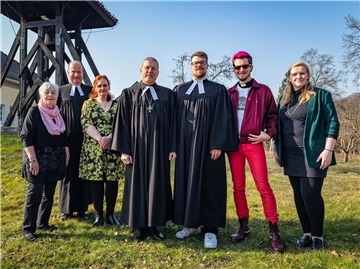 Sieben Erwachsene haben sich auf einem grünen Hügel zu einem Gruppenfoto aufgestellt. Anlass war die offizielle Amtseinführung eines neuen Pastors.