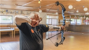 Ein Bogenschütze hält im Training Pfeil und Bogen und zielt auf die Zielscheibe.