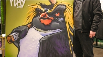Ein Künstler zeigt sein Gemälde von einem gesprayten Pinguin.