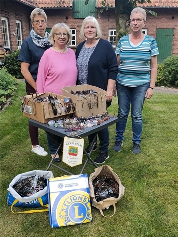 Vier Frauen stehen in einem Garten vor einem Tisch. Darauf und davor liegen Kartons und Tüten voller Brillen.
