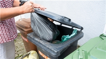 Person wirft eine Mülltüte in eine Restmülltonne.