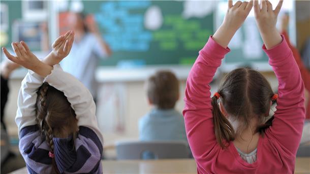 Zwei Schülerinnen melden sich während des Unterrichts in einem Klassenzimmer einer Grundschule. 