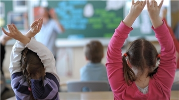 Zwei Schülerinnen melden sich während des Unterrichts in einem Klassenzimmer einer Grundschule. 