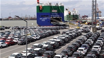 Autos im Hafen stehen vor einem Autotransporter