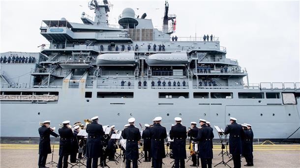 Marineschiff „Frankfurt am Main“ kehrt zurück Der Marinemusikkorps Wilhelmshaven steht an einer Kaimauer, während die „Frankfurt am Main“ in den Hafen einfährt.