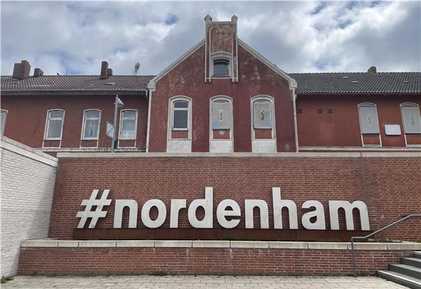 Der moderne Schriftzug "#nordenham" wirkt vor dem heruntergekommenen Bahnhofsgebäude in Nordenham fast schon grotesk.