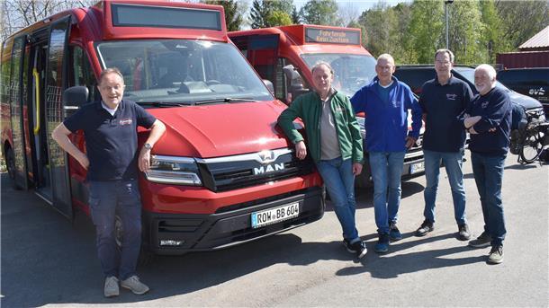 Fünf Männer stehen vor einem kleinen roten Bus.