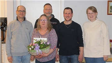 Zwei Frauen und drei Männer stehen nebeneinander. Eine Frau hält ein Blumengesteck in den Händen.