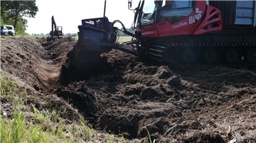 Ein Pistenbully verfüllt einen Graben mit Torf.