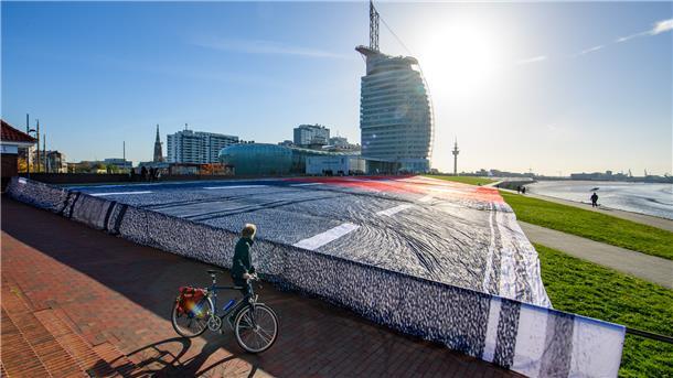 Der Protest gegen den Ausbau der A20 nimmt am Mittwochvormittag Formen an. Die Demonstranten haben ein riesiges Protestbanner über den Boden am Deich gelegt.