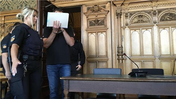 Mann mit verdecktem Gesicht wird von Justizbeamten hereingeführt.