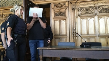 Mann mit verdecktem Gesicht wird von Justizbeamten hereingeführt.