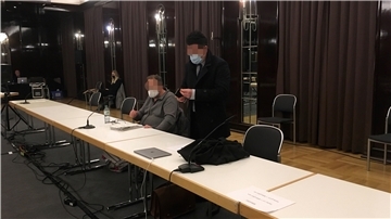 Zwei Personen, der Angeklagte und sein Anwalt, an einer langen Tischreihe.
