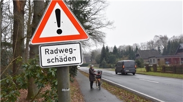 Das Foto zeigt ein Schild mit dem Hinweis Radwegschäden. 