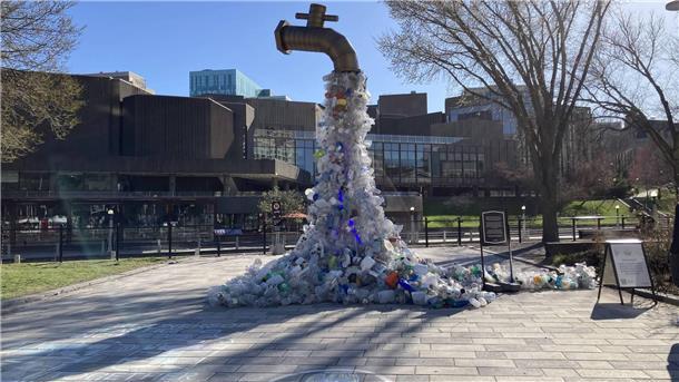 Kunstwerk eines großen Wasserhahns aus dem Plastikmüll fließt vor einem Konferenzzentrum