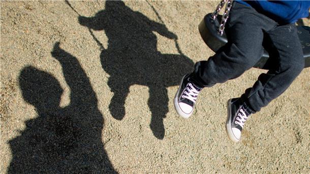 Ämter bei Aufnahme von minderjährigen Geflüchteten am Limit Der Schatten von einem Mann und einem schaukelnden Kind auf einem Spielplatz.