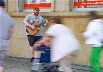 Ein Mann steht auf dem Fußweg und spielt Gitarre. Menschen laufen an ihm vorbei. Mike Meinert ist Straßenmusiker in Bremerhaven.