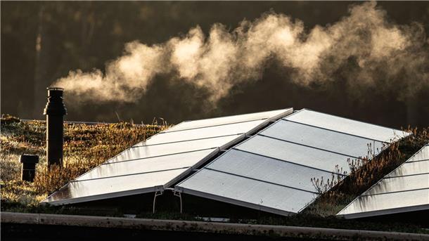 Der Schornstein einer Gasheizung dampft auf dem Flachdach eines Reihenhauses.